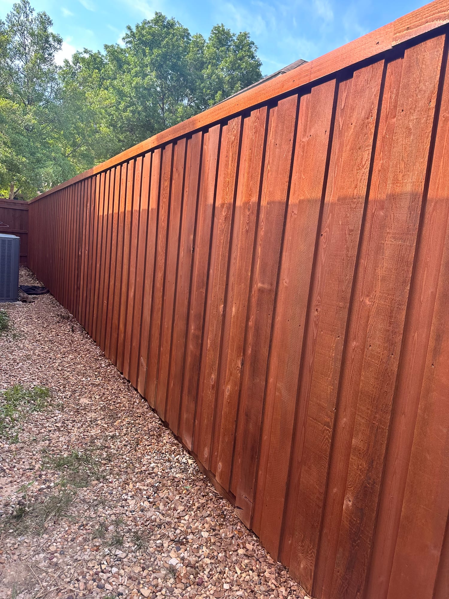 Reddish-brown stained wood fence running along a gravel side yard