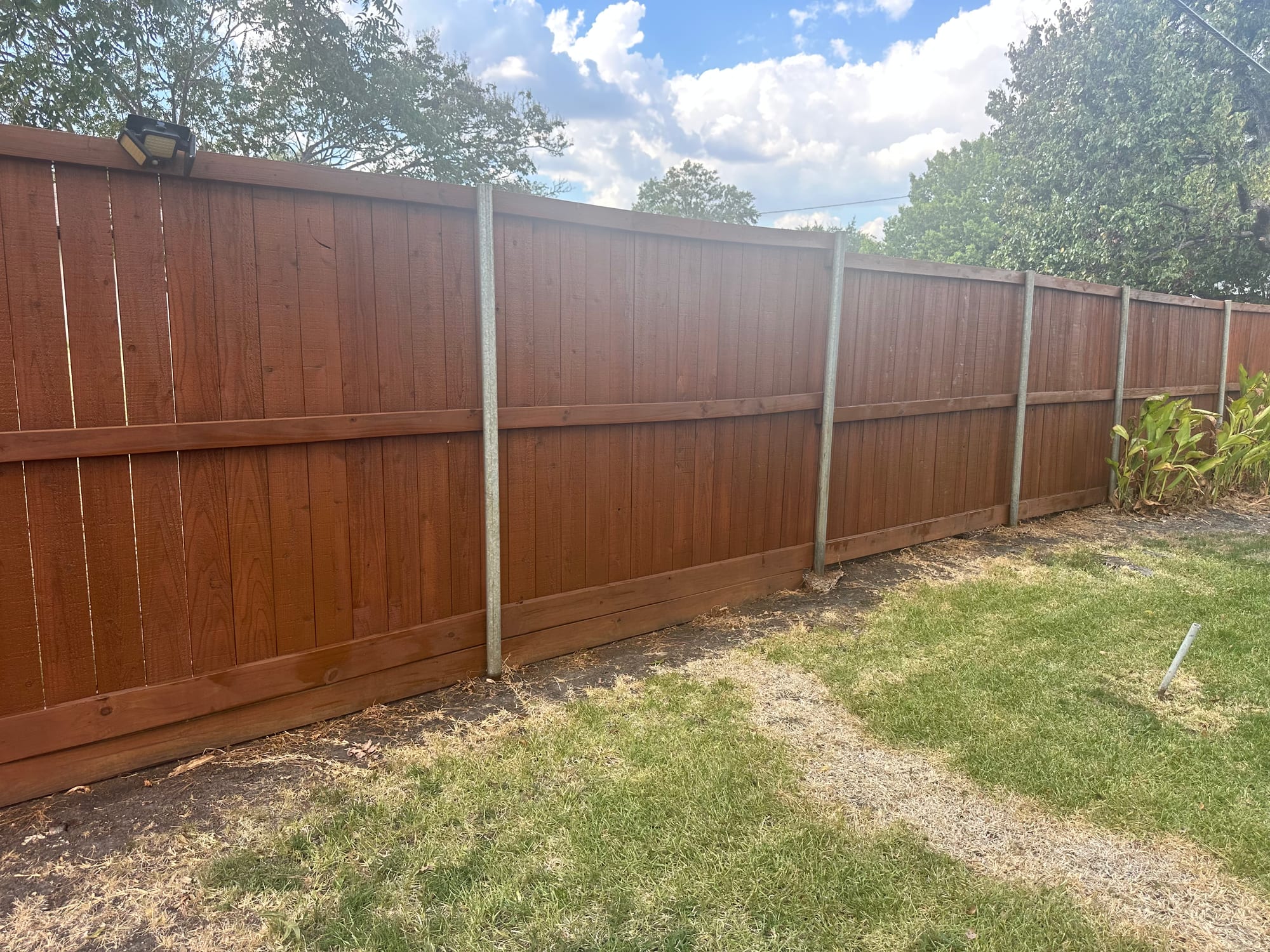 Long stained wood privacy fence with horizontal rails and galvanized metal posts beside a backyard lawn