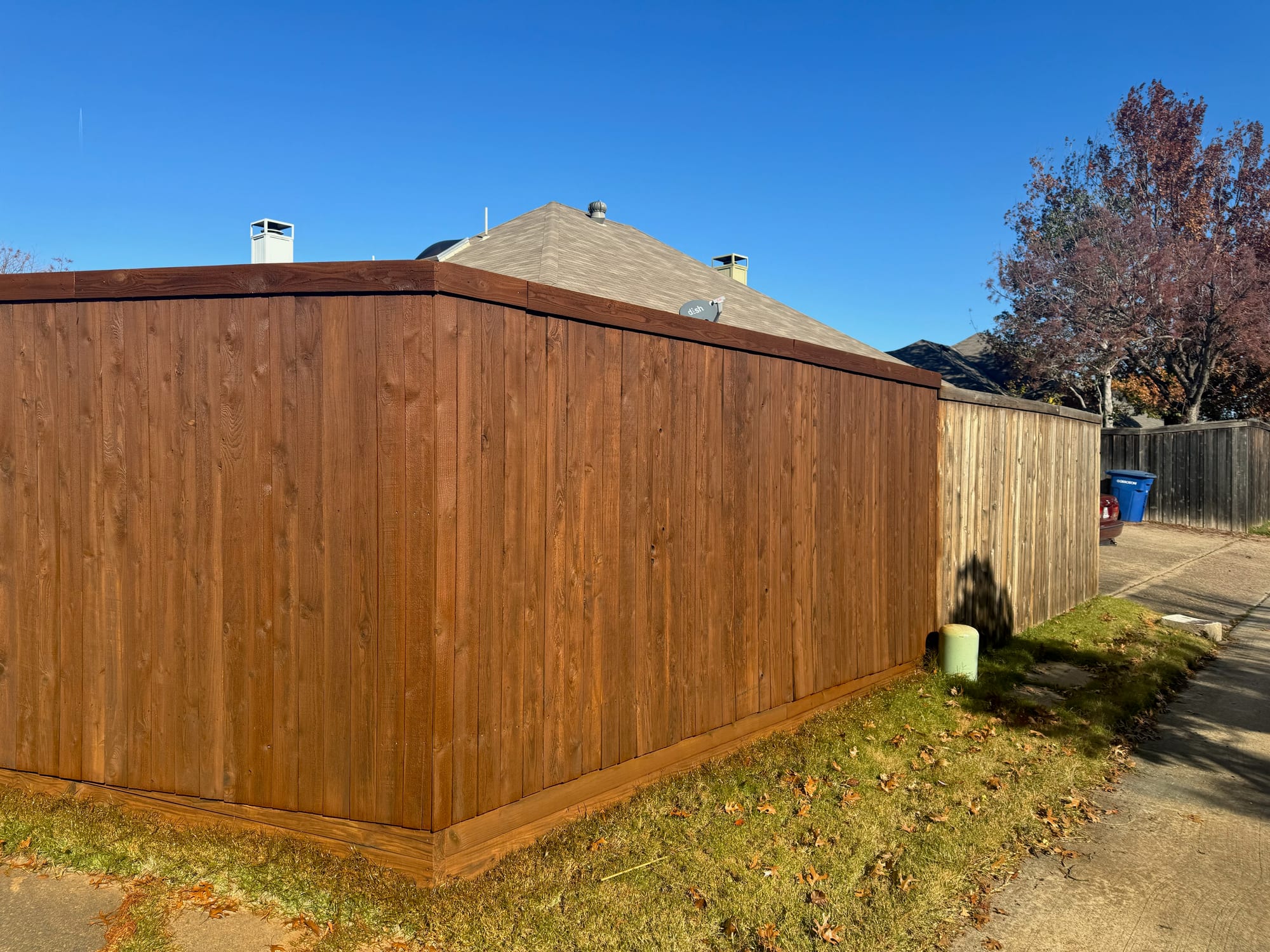 Corner of a warm brown stained wood fence with a top cap under a clear blue sky